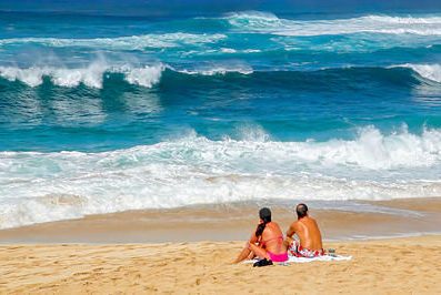 Two beach goers sitting at Sunset Beach on the island of Oahu watching the surf